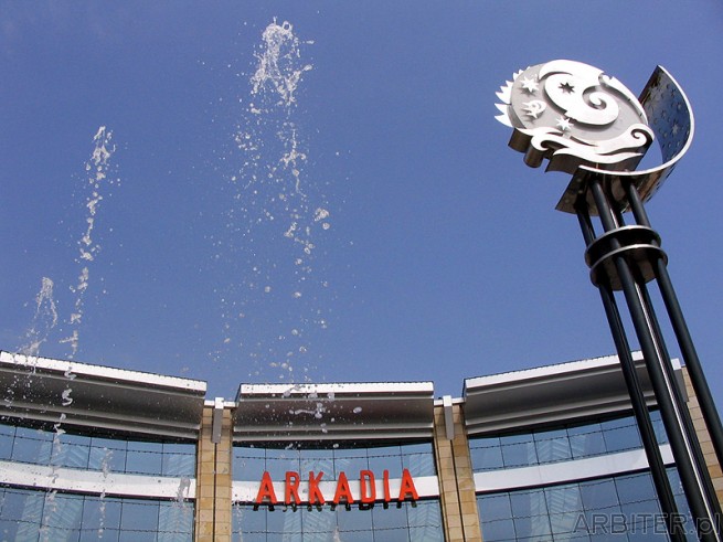 Tryskająca fontanna. W prawej części fotografii logo Arkadii