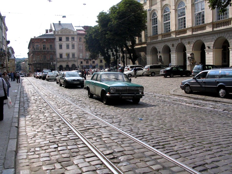 Uliczka na Rynku Lwowskim. Samochody parkują na środku ulicy, niekiedy jadą tramwaje